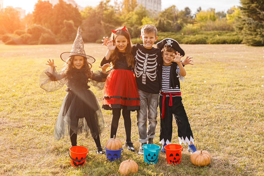 Adorable little kids in carnival costumes standing with scary hands and pumpkins hugging and looking at camera in autumn